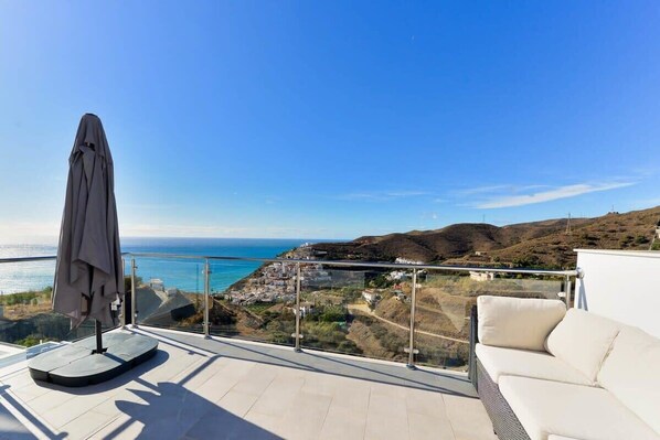 A balcony with a view of the sea, a white sofa, and a covered table.