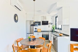 Une cuisine moderne avec des meubles blancs, un Ăźlot central et un coin repas comprenant des chaises en bois et une table ronde.