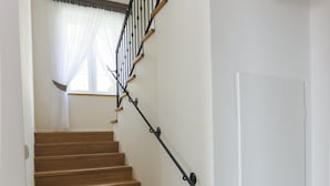 A wooden staircase with a black handrail leading to a white door.