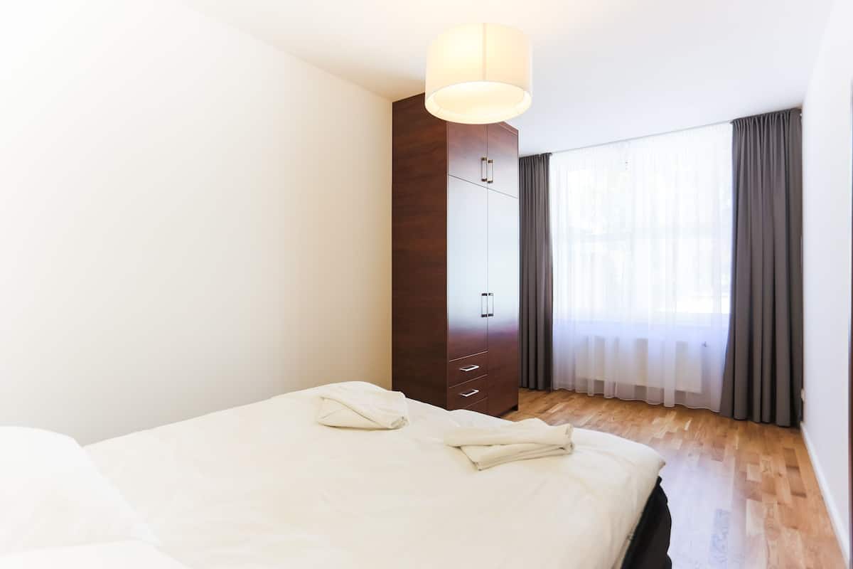 Una habitación de hotel con cama, armario, lámpara colgante y ventana con cortinas.