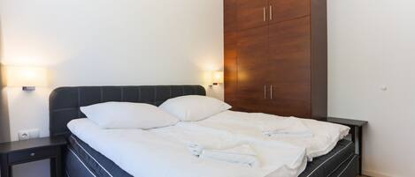 Una cama doble con ropa blanca de cama bien tendida, un cabecero oscuro y un armario de madera con dos puertas.