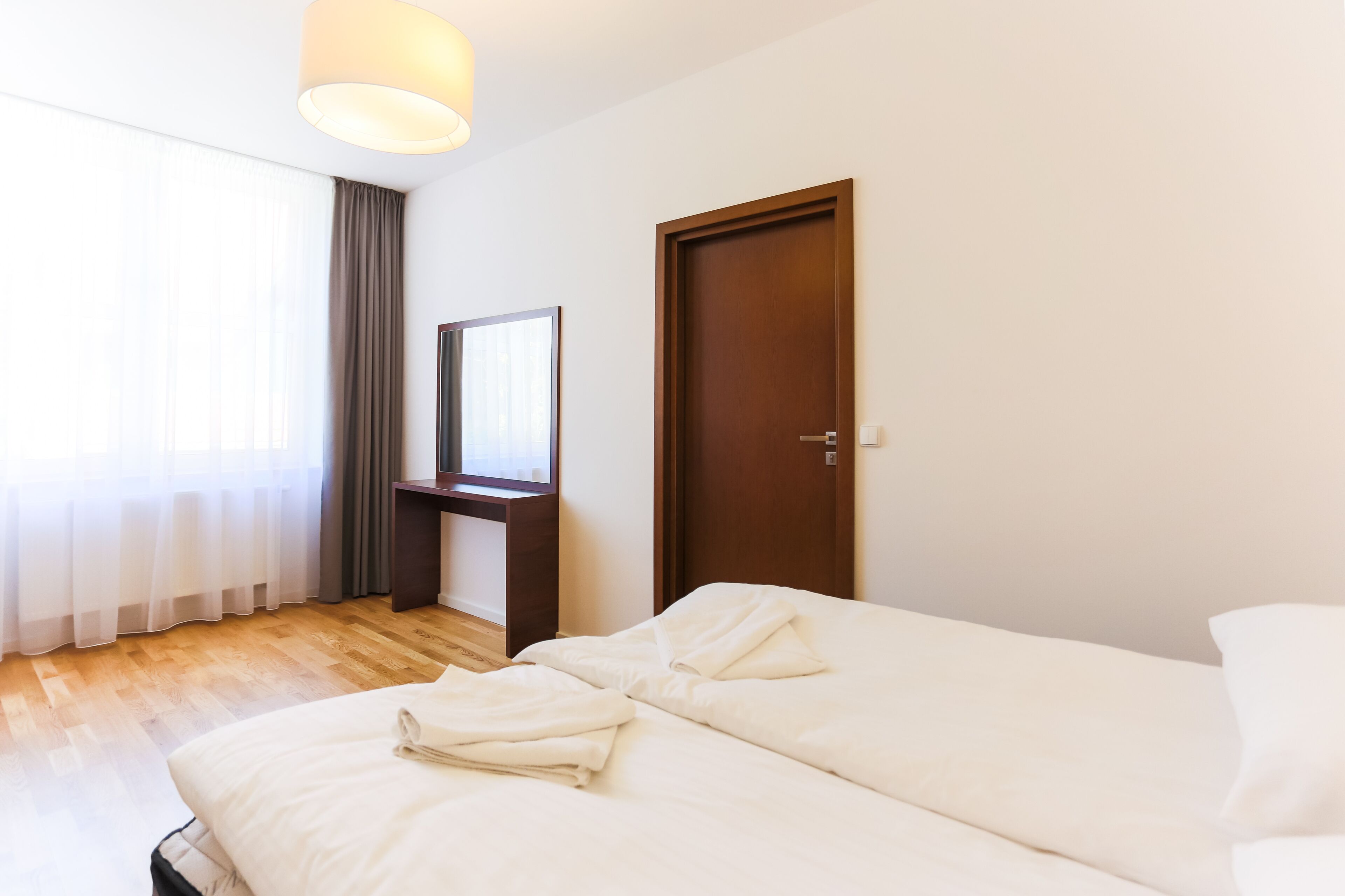 Una habitación de hotel con una cama, un escritorio de madera, un espejo y una puerta.
