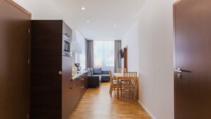 A modern kitchen with dark wooden cabinets, a dining area with a wooden table and chairs, and a grey sofa.