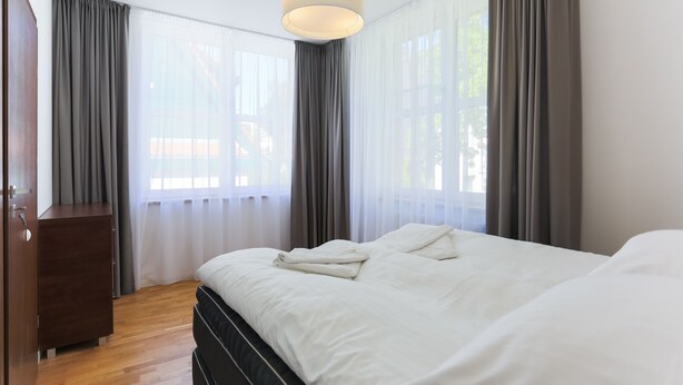 A bedroom with a bed, a wooden dresser, and a large window with curtains.