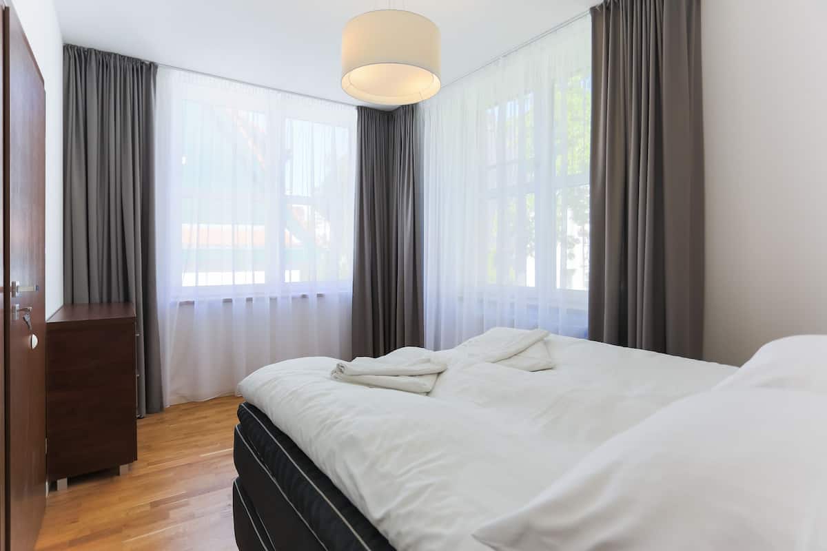 Un dormitorio con cama, cómoda de madera y una ventana grande con cortinas.