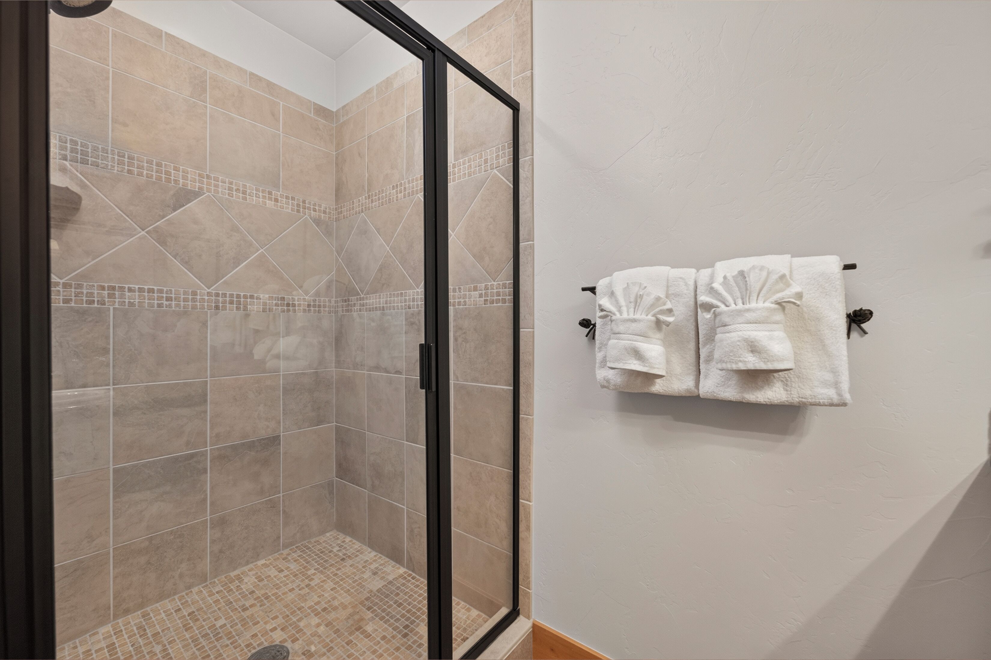 A shower area with a glass door, tiled walls, and a tiled floor. There are two towels hanging on a towel rack.