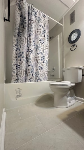 Ein Badezimmer mit Toilette, einer Duschkabine mit tropischem Blattmuster, einem Spiegel und einem Handtuchhalter.