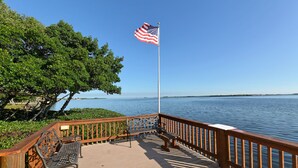 A wooden deck with a metal bench and a flagpole with an American flag.