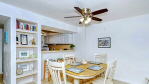 A dining area with a round table, white chairs, and a ceiling fan.