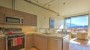 A modern kitchen with stainless steel appliances, wooden cabinets, and a large window offering a mountain view.
