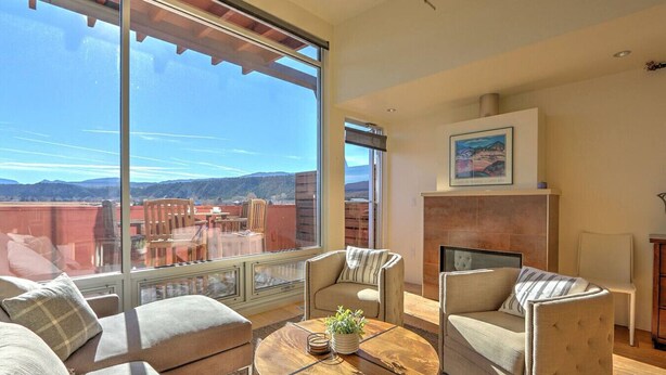 A spacious living room with a large window offering a view of the mountains. There is a fireplace, comfortable seating, and a coffee table with a plant.