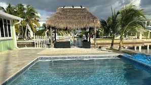 Une piscine d’eau cristalline, avec en arrière-plan une structure surmontée d’un toit de chaume.