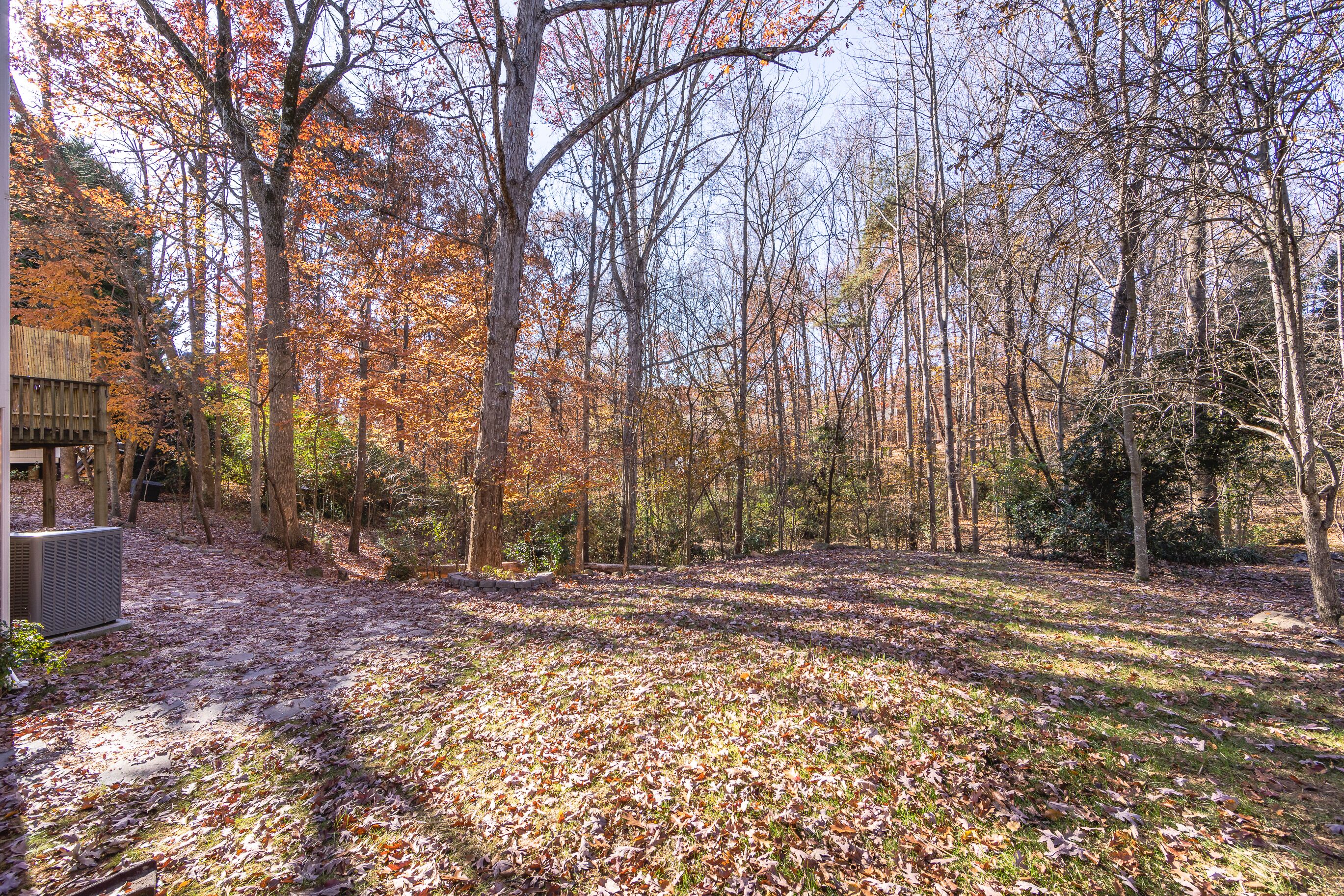 A forested area with a dirt path and a building with a large air conditioning unit.