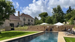 A swimming pool with lounge chairs and umbrellas, surrounded by a stone wall and a stone building. - Gîte la Porterie - Clos des Dames de Lancharre (Chapaize)