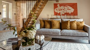A living room with a wooden staircase, a patterned sofa, and a decorative wall piece. - Gîte la Porterie - Clos des Dames de Lancharre (Chapaize)