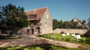 A stone building with a tiled roof, a paved entrance, and a garden with white chairs. - Gîte la Porterie - Clos des Dames de Lancharre (Chapaize)