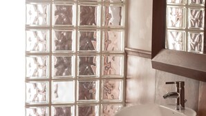 Un bagno con un lavandino bianco, uno specchio e una finestra con vetri decorati.