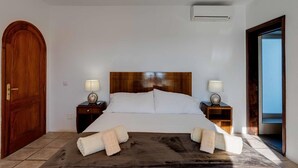 Una camera da letto con un letto grande, una testiera in legno, due comodini con lampade, una porta in legno e vista attraverso una porta aperta.