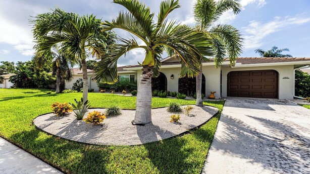 Una propiedad residencial con césped cuidado, palmeras y un garaje.