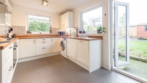 A modern kitchen with white cabinets, a washing machine, and a large window. - Charming Cardoon Cottage in Beautiful Village (Crieff)