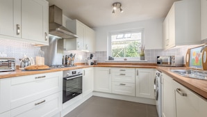 A modern kitchen with white cabinets, a wooden countertop, a built-in oven, a dishwasher, and a window providing natural light. - Charming Cardoon Cottage in Beautiful Village (Crieff)
