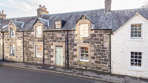 A row of stone buildings with multiple windows and doors, some with shutters, and a clear sky above. - Charming Cardoon Cottage in Beautiful Village (Crieff)