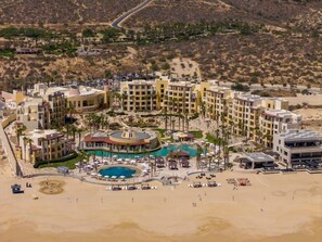 A resort with multiple buildings, a central pool, and a beach area.