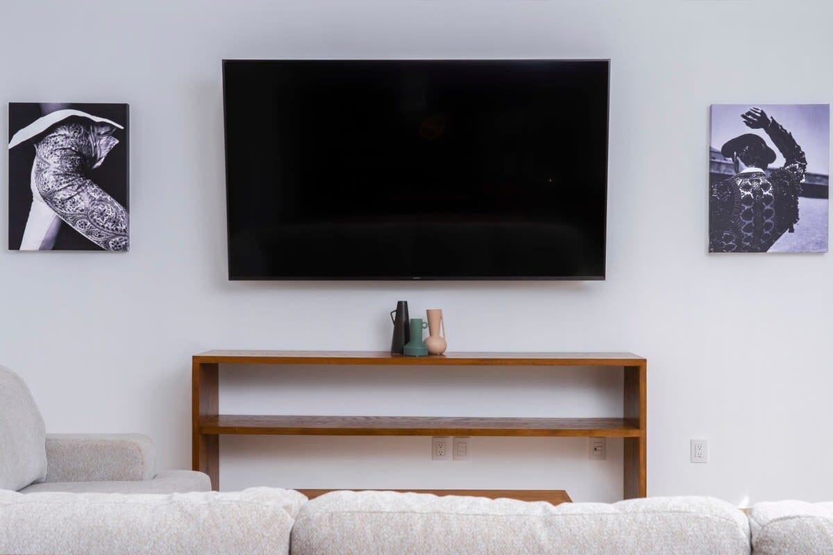Una sala de estar moderna con un televisor de pantalla plana montado en la pared, un mueble de televisión de madera con adornos y un sofá.