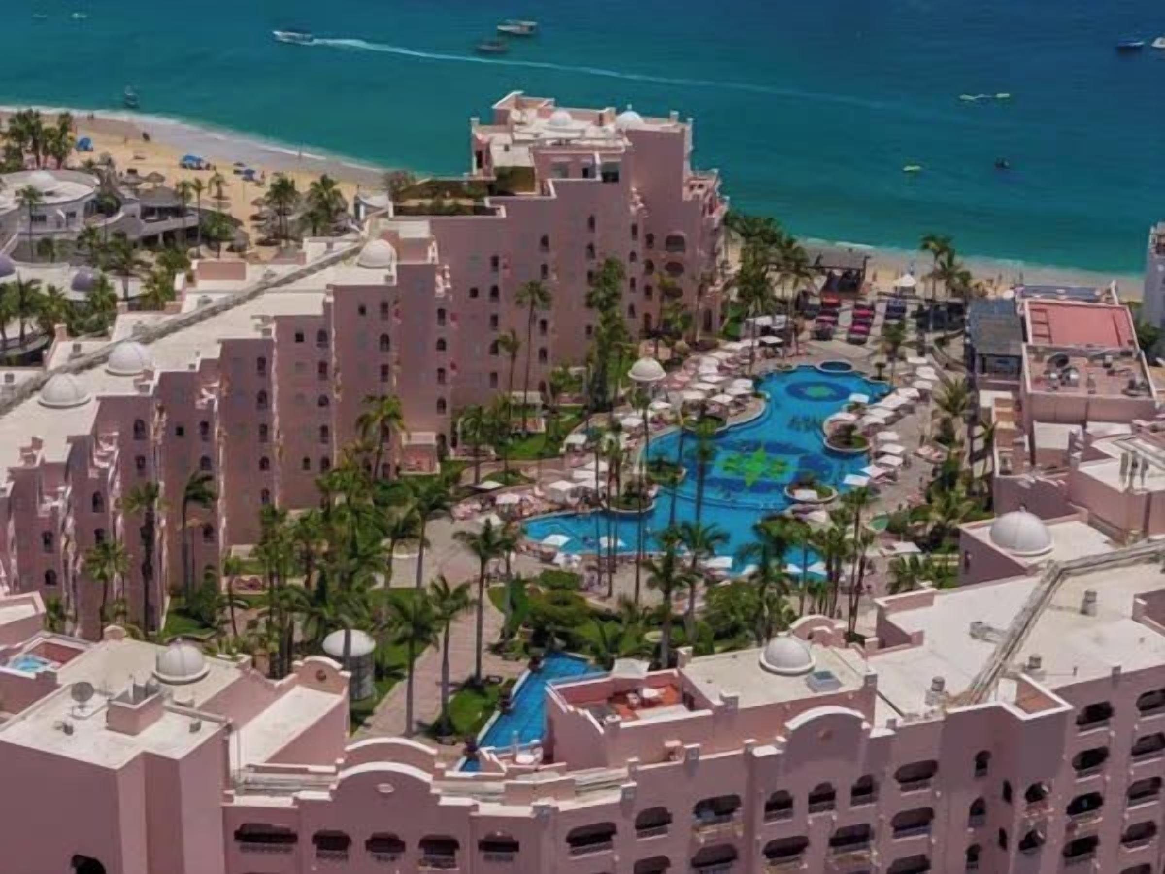 A resort with a central swimming pool, multiple buildings, and a beach.