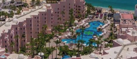 A resort with a central swimming pool, multiple buildings, and a beach.