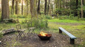 A forest campsite with a fire pit, two folding chairs, and a bench. - Quantum Field by Tiny Away (Toolangi)
