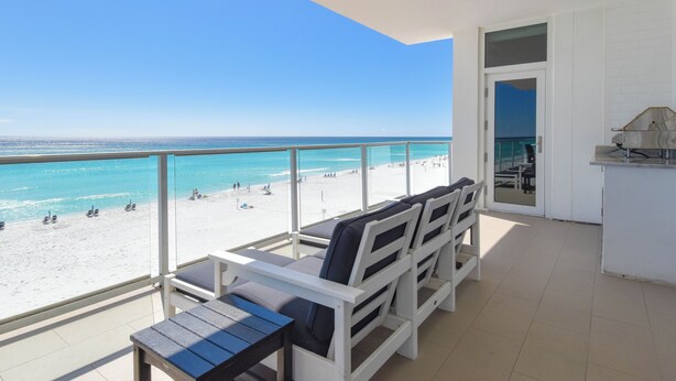 A balcony with a view of the beach, white furniture, and a door leading to an interior space. - Luxurious Beachfront Condo w/ Beach Service & Rooftop Pool in Destin! 🌊☀💙 (Destin)