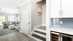 Una sala de estar moderna con un sofá y una mesa de centro, una escalera que lleva a una cocina con armarios blancos y un salpicadero de azulejos.