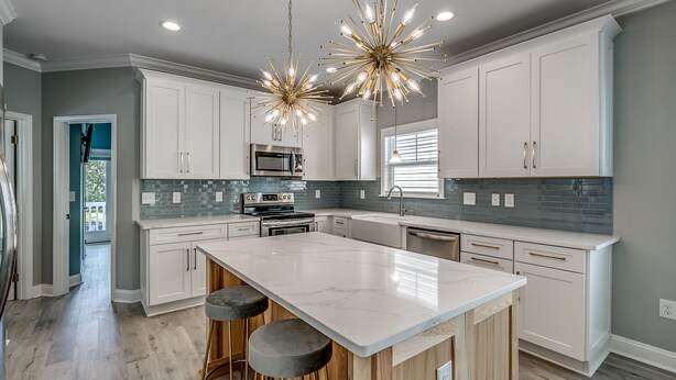 Una cocina moderna con armarios blancos, una isla grande, electrodomésticos de acero inoxidable y un candelabro original.