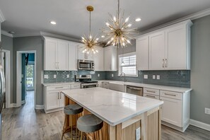 Une cuisine moderne avec des armoires blanches, un grand îlot central, des appareils en acier inoxydable et un lustre original.