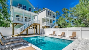 Una casa de dos pisos con piscina, mobiliario exterior y una terraza de madera.