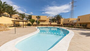 A swimming pool with steps leading into it, surrounded by palm trees and a building with a beige facade. - Private Terrace Home - Pool - Wifi (Costa Calma)