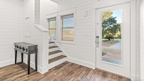 Un interior blanco con una escalera, una pequeña mesa con cajones y una puerta con la etiqueta 'BEACH'.