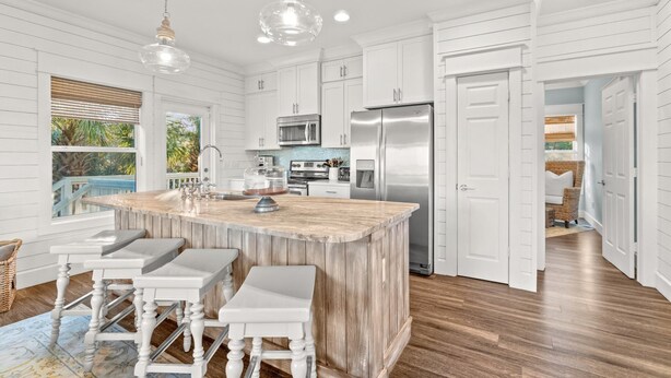 Una cocina amplia con una isla grande, armarios blancos, electrodomésticos de acero inoxidable y piso de madera.