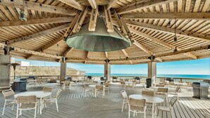 A covered outdoor patio with wooden beams and a central hanging light fixture. Tables and chairs are arranged for dining or socializing. - Sunrise gulf view/beach front condo! Enjoy one free beach chair set up each day (Destin)