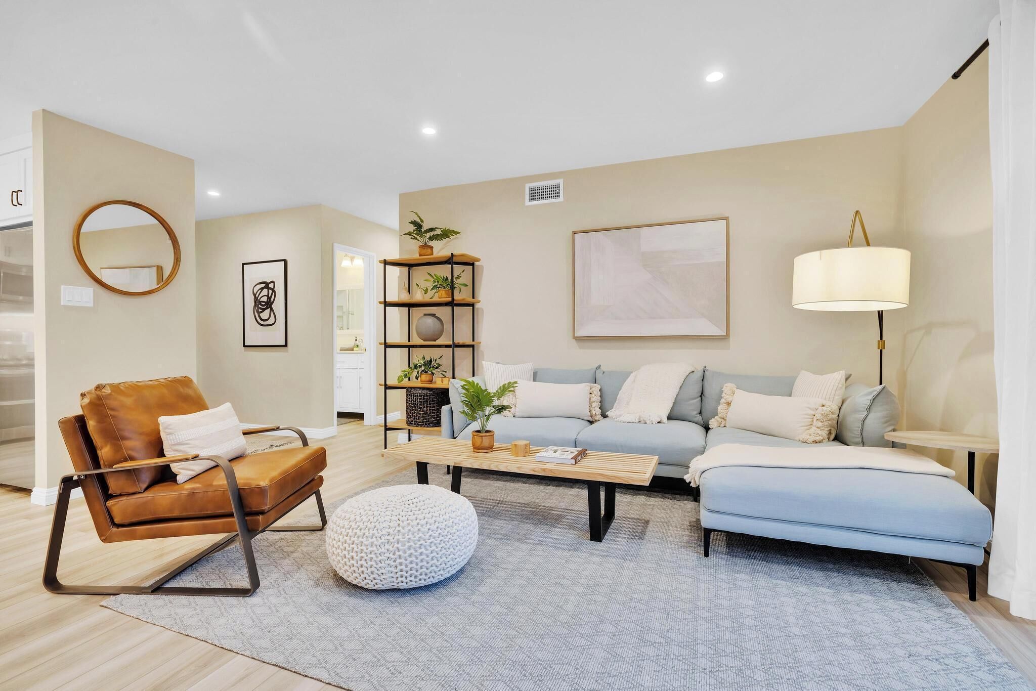 Una sala de estar moderna con un sillón de cuero marrón, un sofá azul claro, un otoman redondos y una mesa de centro de madera.