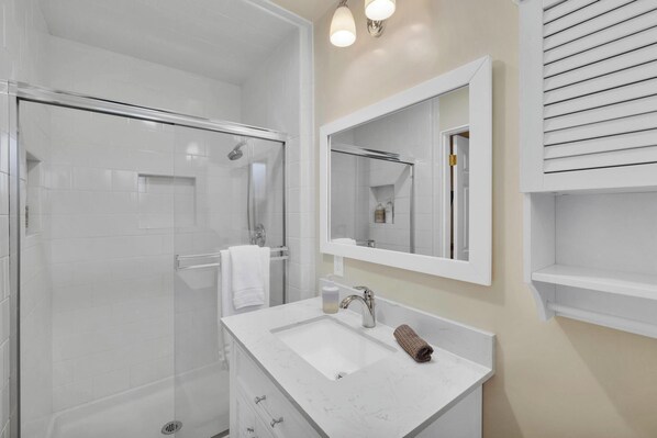 A modern bathroom with a glass shower enclosure, a white sink, and a mirror above it.