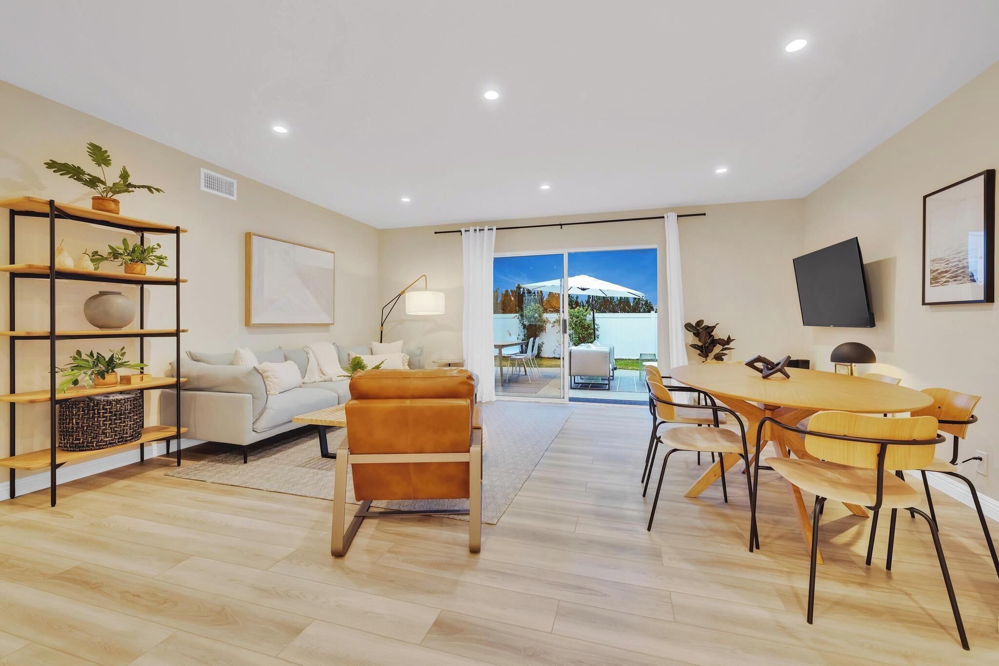 Una sala de estar moderna con un sofá, un sillón de cuero marrón, una mesa de comedor con sillas y un televisor montado en la pared.