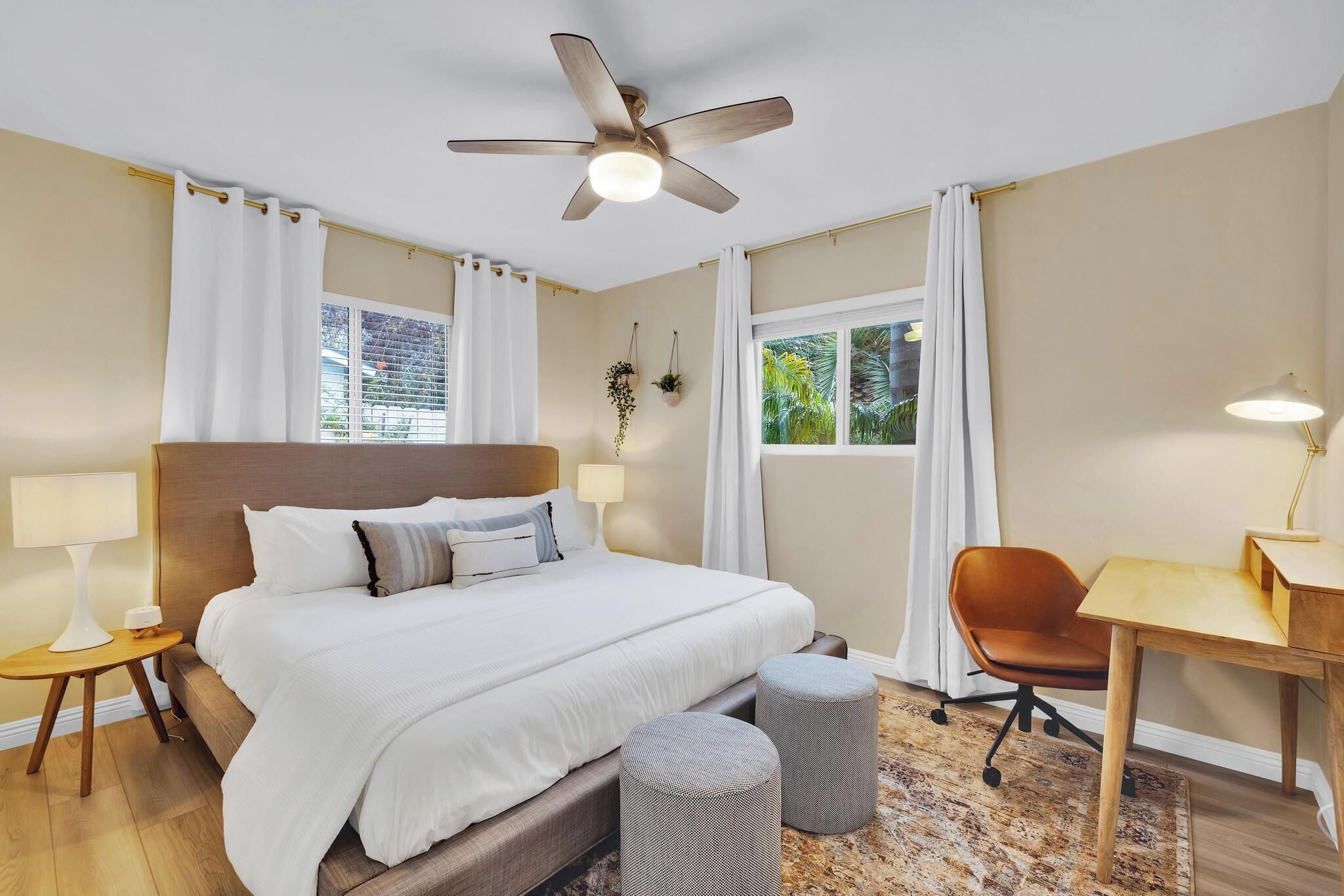 Una habitación de hotel con cama, escritorio, silla, ventilador de techo y ventana con cortinas.
