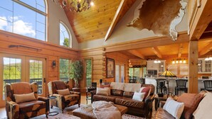L’intérieur de cette vaste cabane en rondins offre un grand espace de vie, un plafond en bois et une vue sur l’extérieur grâce à de grandes fenêtres.