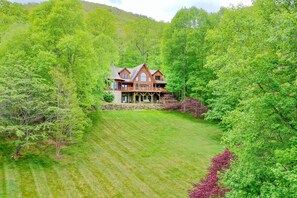 A large, two-story wooden house with a stone foundation, surrounded by lush green trees and a well-maintained lawn. - Sweetwater Lodge - Luxury Log Cabin Rental (Canton)