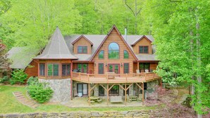 Une cabane en rondins avec des fondations en pierre, une terrasse en bois et un grand porche à l’avant.