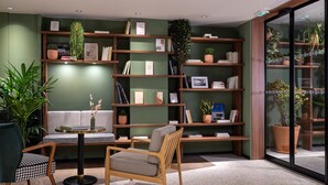 Una sala de lectura moderna con paredes verdes, estanterías de madera, una mesa redonda y asientos cómodos.