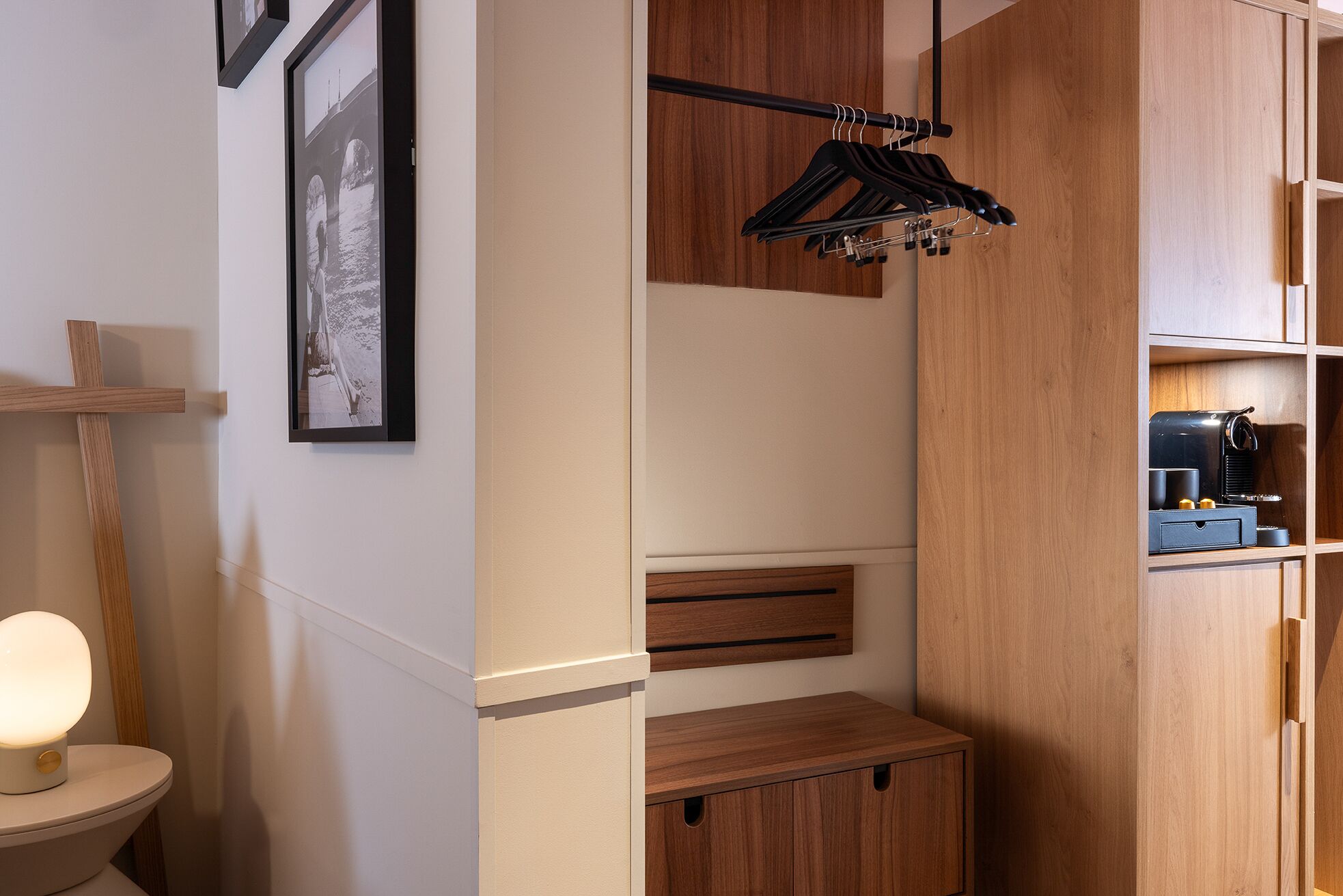 A compact bathroom with a wooden vanity, a hanging clothes rack, and a framed picture on the wall.