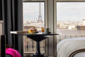 A hotel room with a view of the Eiffel Tower, a breakfast tray with croissants and orange juice, and a bed with a white blanket. - Hôtel Les Artistes (Paris)